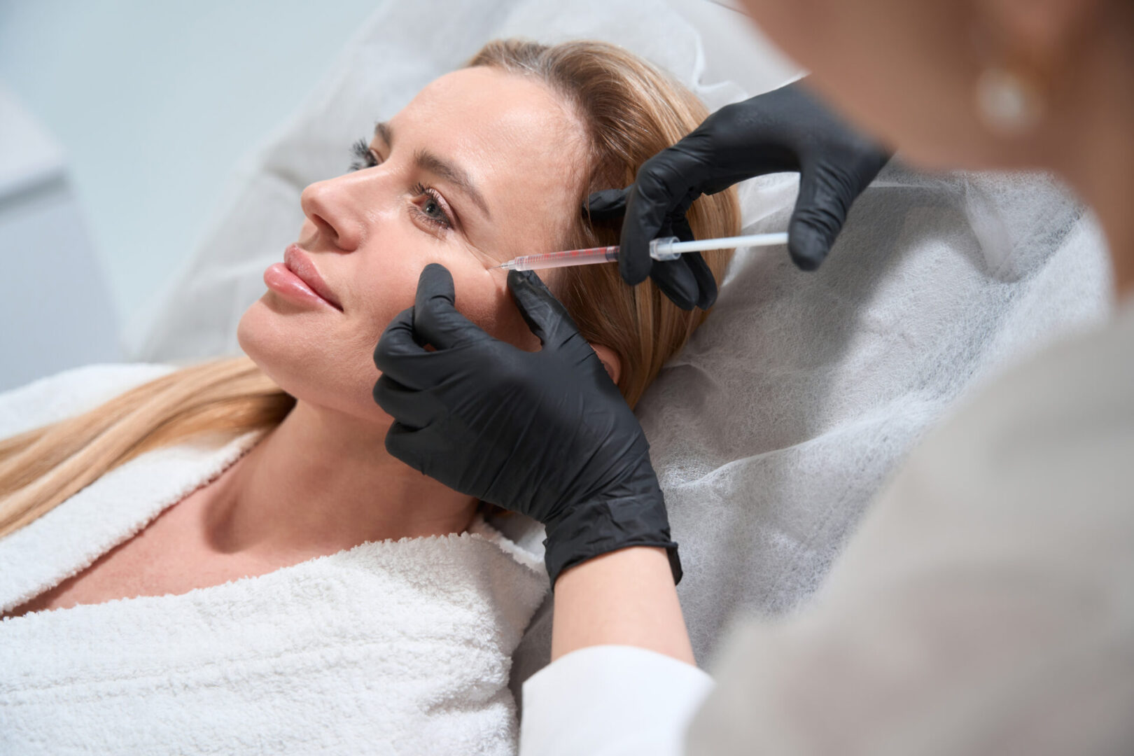 Female blonde gets a rejuvenating injection in her cheeks, an esthetician uses a thin needle